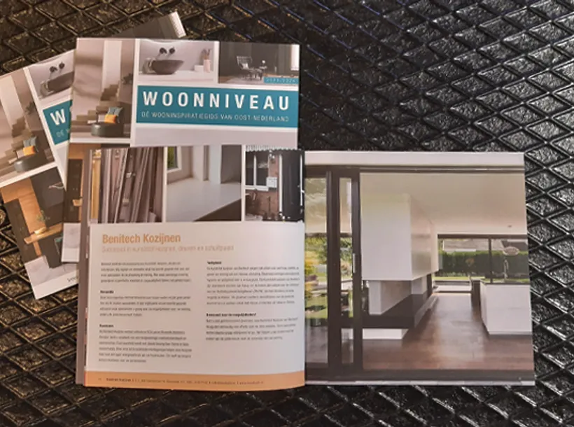 Drie magazines woonniveau op tafel, twee gesloten en één open met artikel over Benitech Kozijnen