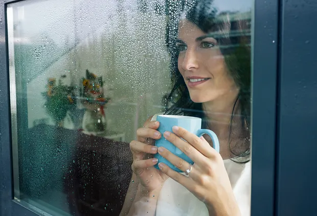 Vrouw met kop drinken kijkt genietend naar buiten door raam met kunststof kozijnen