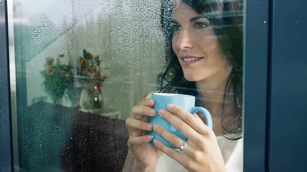 Vrouw met kop drinken kijkt genietend naar buiten door raam met kunststof kozijnen