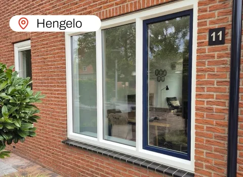 Witte kuststof kozijnen met blauw raam in gevel woning