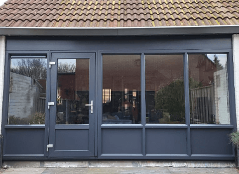 Antracietgrijze kunststof achterdeur met daarnaast 1 kozijn links en 3 kozijnen rechts