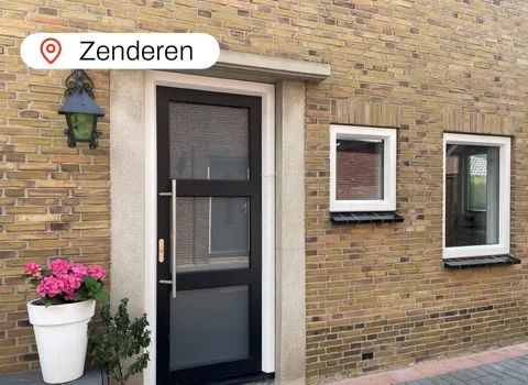 Stenen gevel met antracietgrijze kunststof voordeur en twee kleine witte ramen