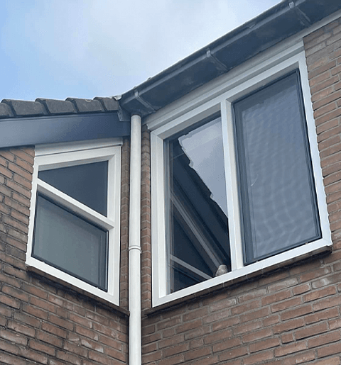 Stenen gevel woning met hoek, twee witte kunststof kozijnen links en rechts
