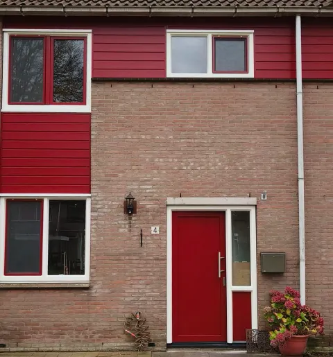 Rijtjeshuis met witte kunststof kozijnen en rode kunststof ramen, gevelbekleding en voordeur