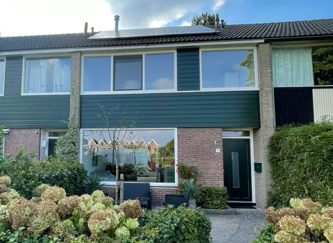 Voorgevel rijtjeswoning met witte kunststof kozijnen en groene kunststof ramen, voordeur en gevelbekleding