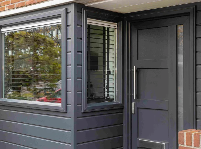 Begane grond voorgevel woning met antracietgrijze kunststof kozijnen, gevelbekleding en voordeur